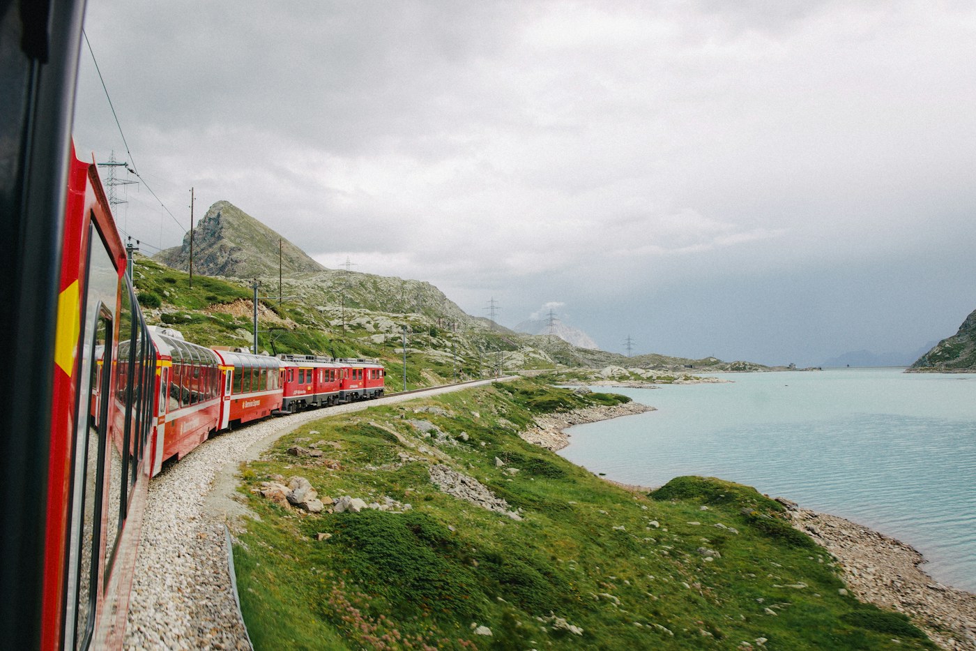 A red train curves along the shore of an alpine lake on Switzerland’s Bernina route
